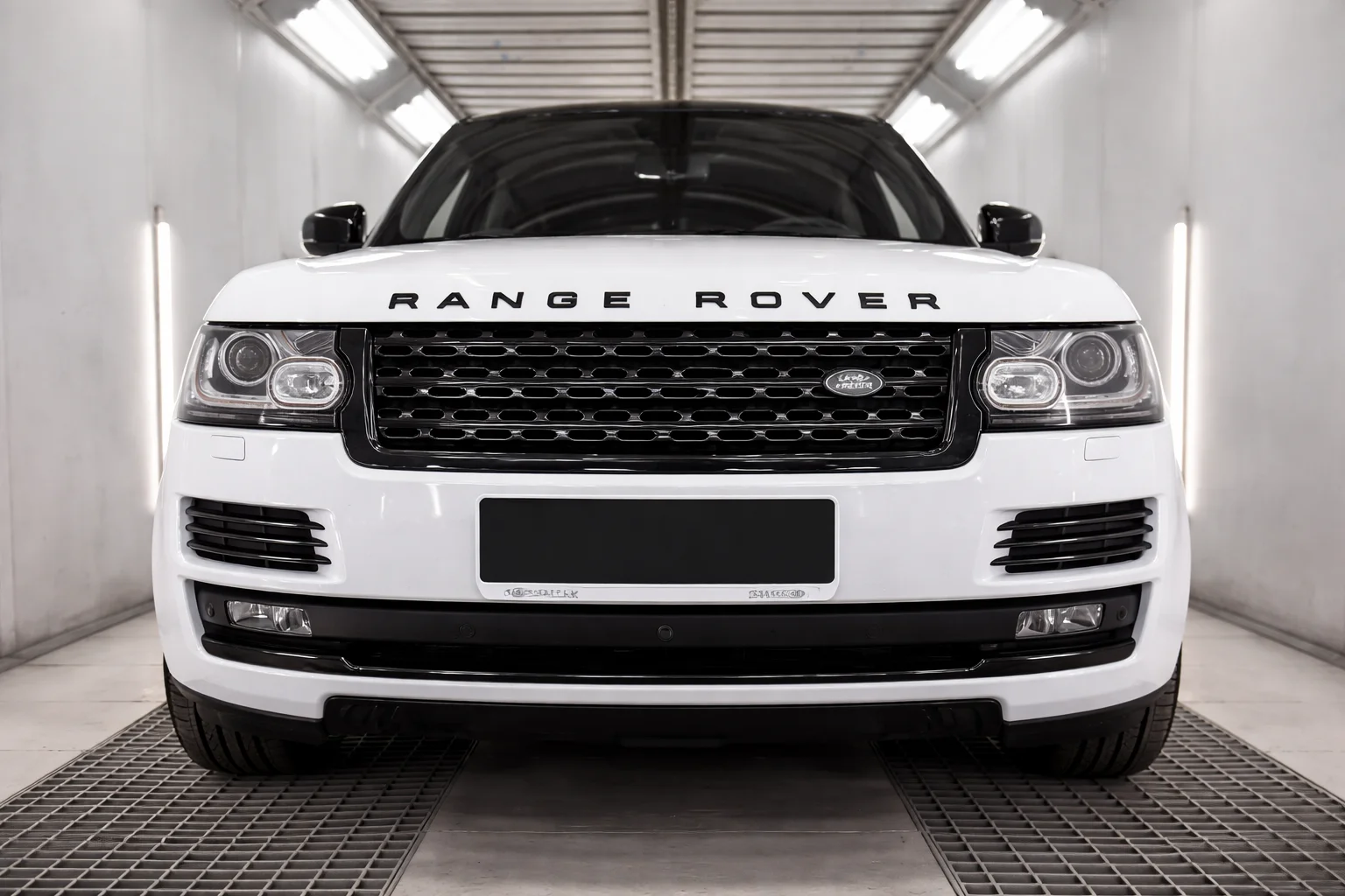 Front view of a white Range Rover positioned inside a professional range rover repair shop, showcasing the vehicle under bright workshop lighting during inspection or servicing.