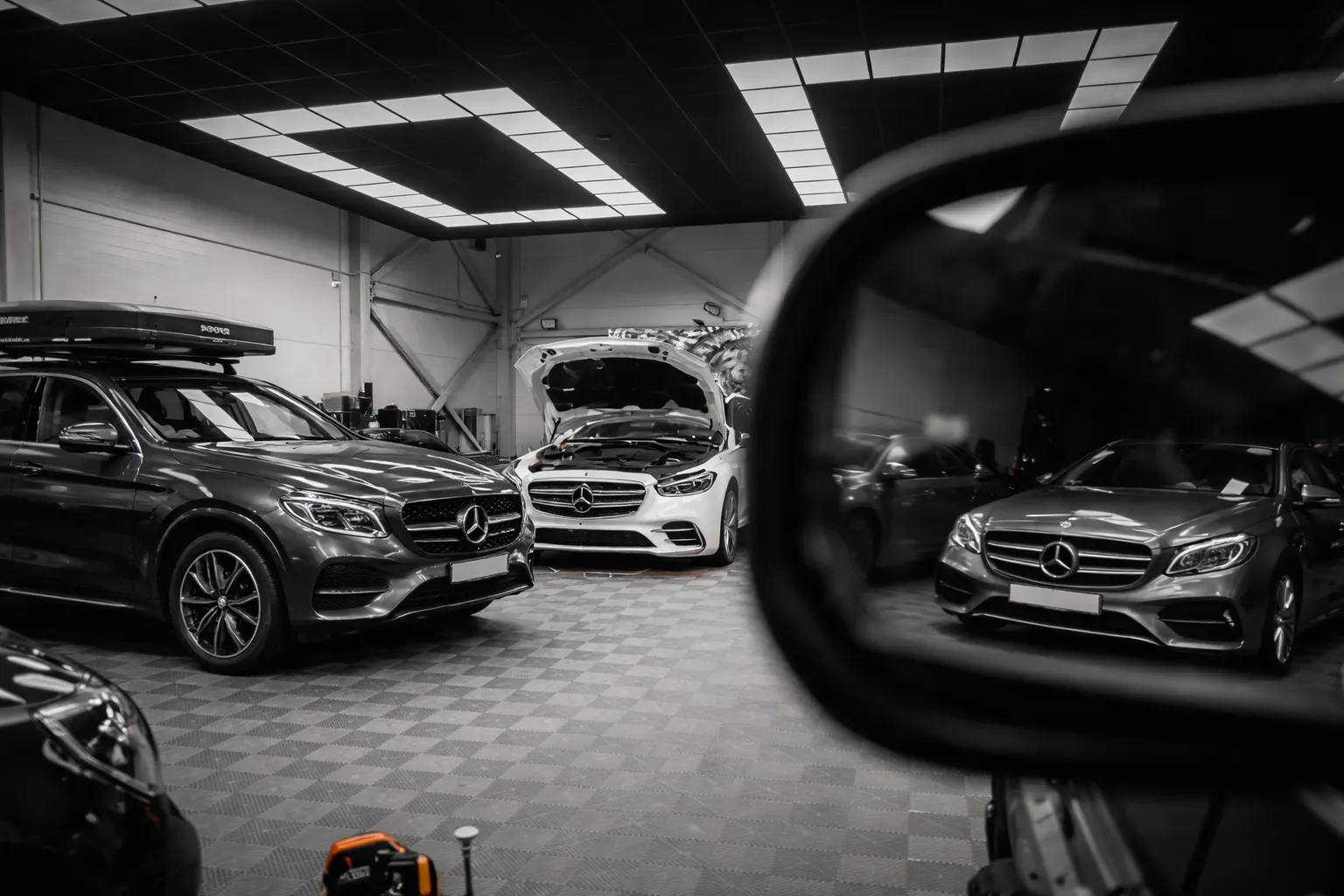 Multiple Mercedes vehicles inside a modern automotive workshop with one car’s hood open for inspection, representing professional german car repair dubai services for luxury vehicle diagnostics and maintenance.
