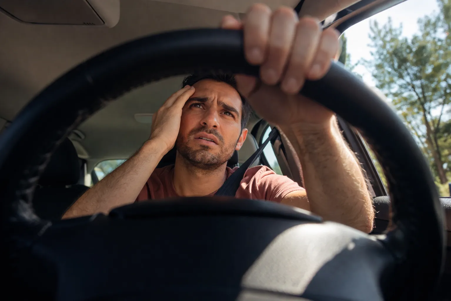 Frustrated man driving and holding his head while gripping the steering wheel, concerned and wondering, “why is my car making a clicking noise?”
