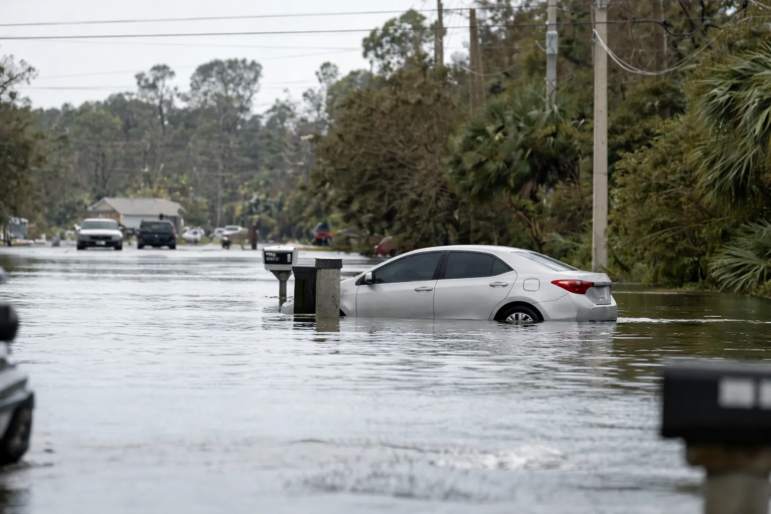 Car partially submerged in floodwater on a residential street, highlighting the urgent need for the best flooded car damage repair near me after severe water damage.