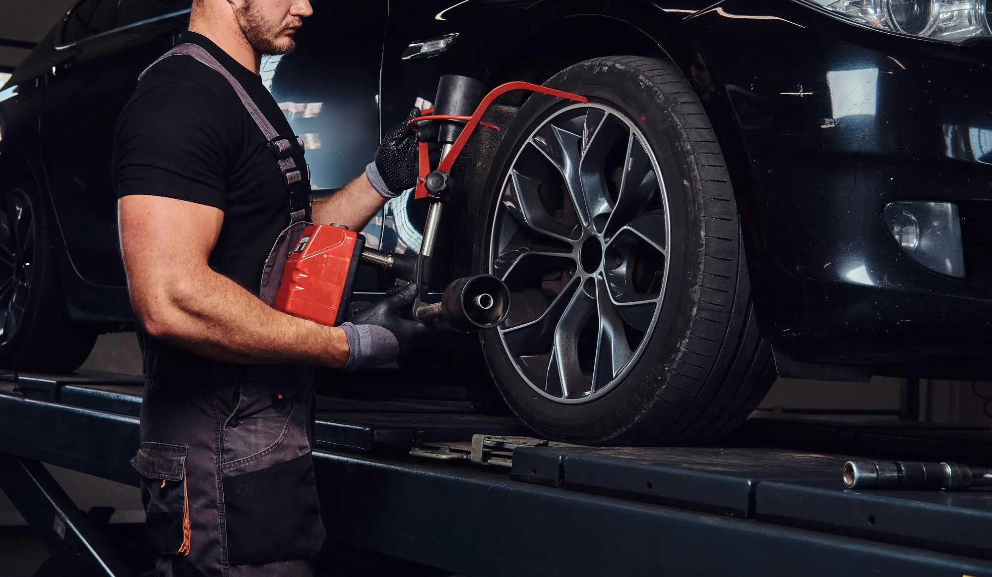 Mechanic performing wheel alignment and suspension adjustment on a black car in a professional workshop, demonstrating expert suspension repair Dubai service for improved vehicle stability and ride comfort.