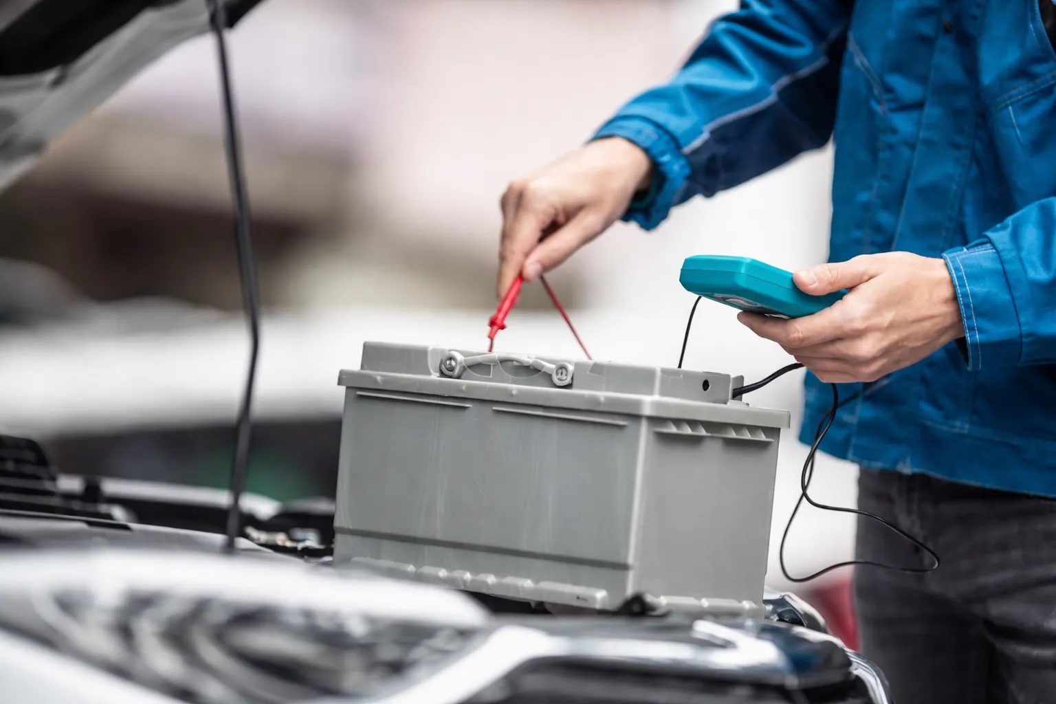 Technician testing a car battery with a multimeter under the hood, helpful visual for car battery near me services and diagnostics in Dubai.