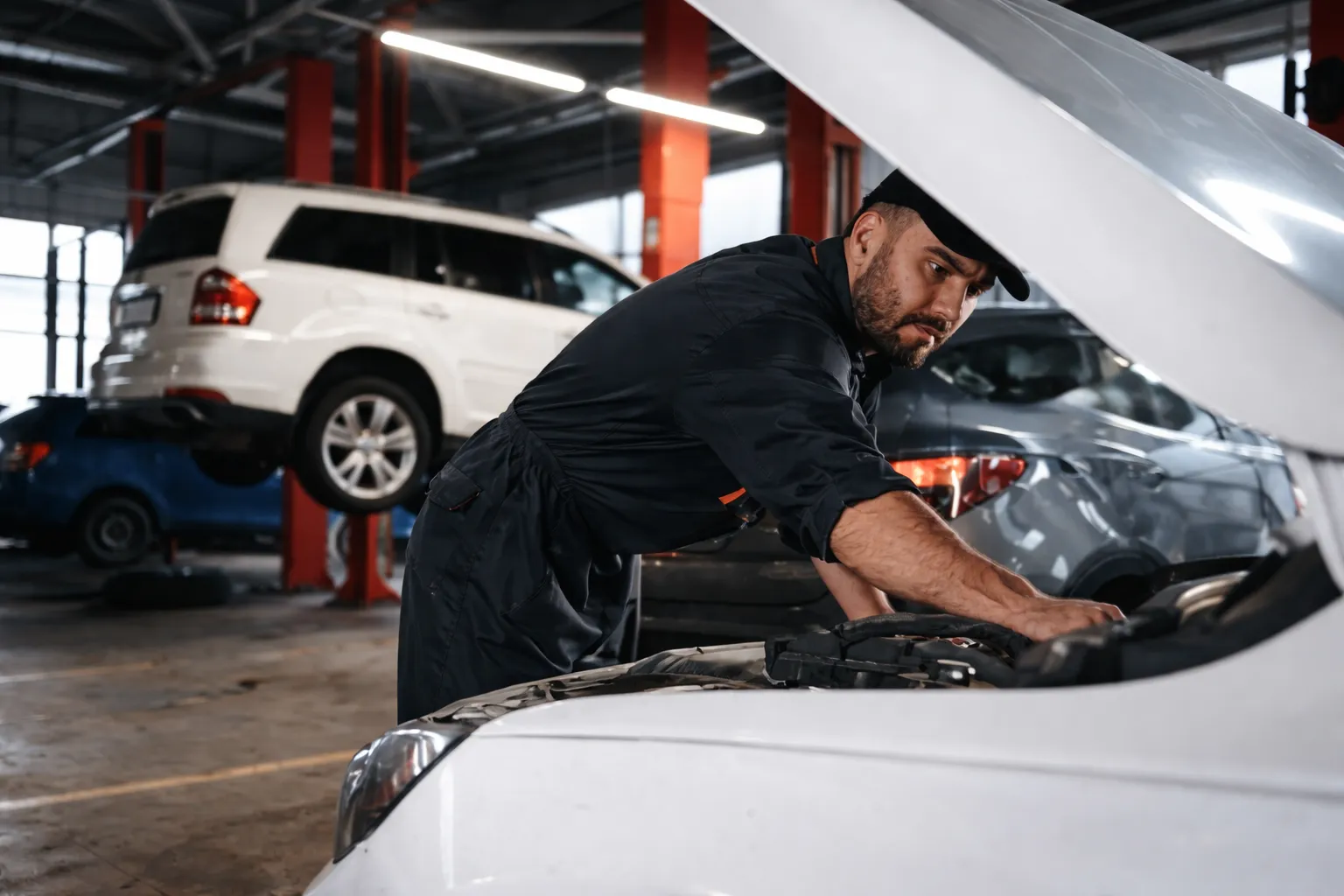 Mechanic inspecting and repairing a car engine inside a modern workshop, representing professional European car repair services.