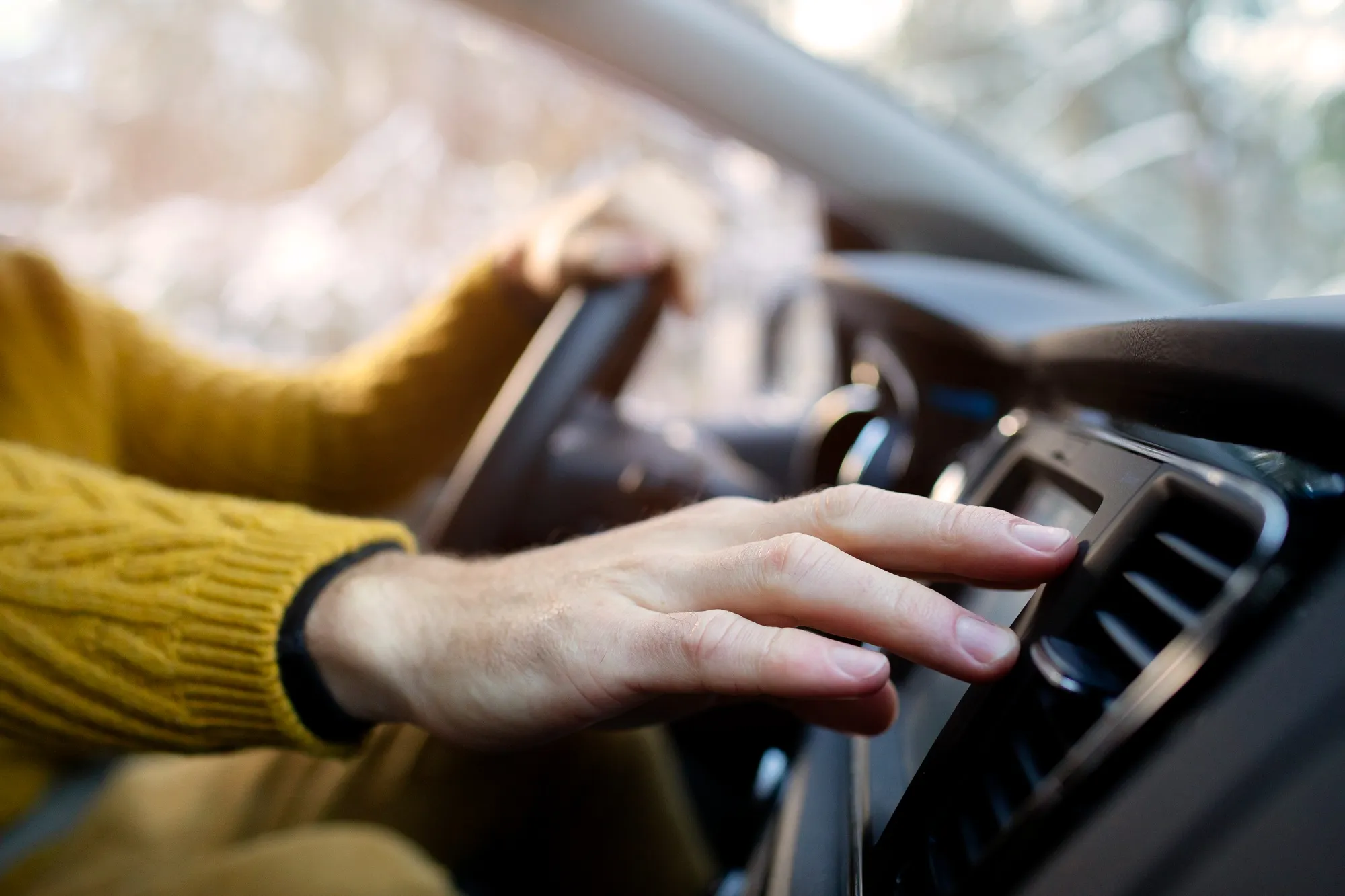 Woman’s hand turning on car air conditioning system inside a vehicle, related to car aircon repair and cooling system maintenance.