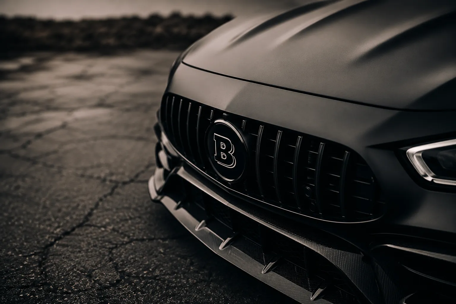 Close-up of a matte black Brabus luxury car front grille with a bold “B” emblem, carbon fiber detailing, and cinematic lighting on a textured road surface; showcasing premium automotive styling and Brabus upholstery service in Dubai.