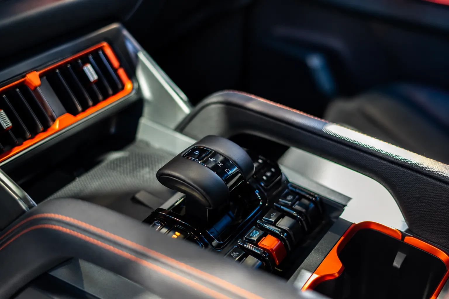 Modern vehicle center console with automatic gear selector, premium black leather interior, illuminated controls, and sporty orange accents designed by a professional transmission specialist in a luxury automotive cabin.