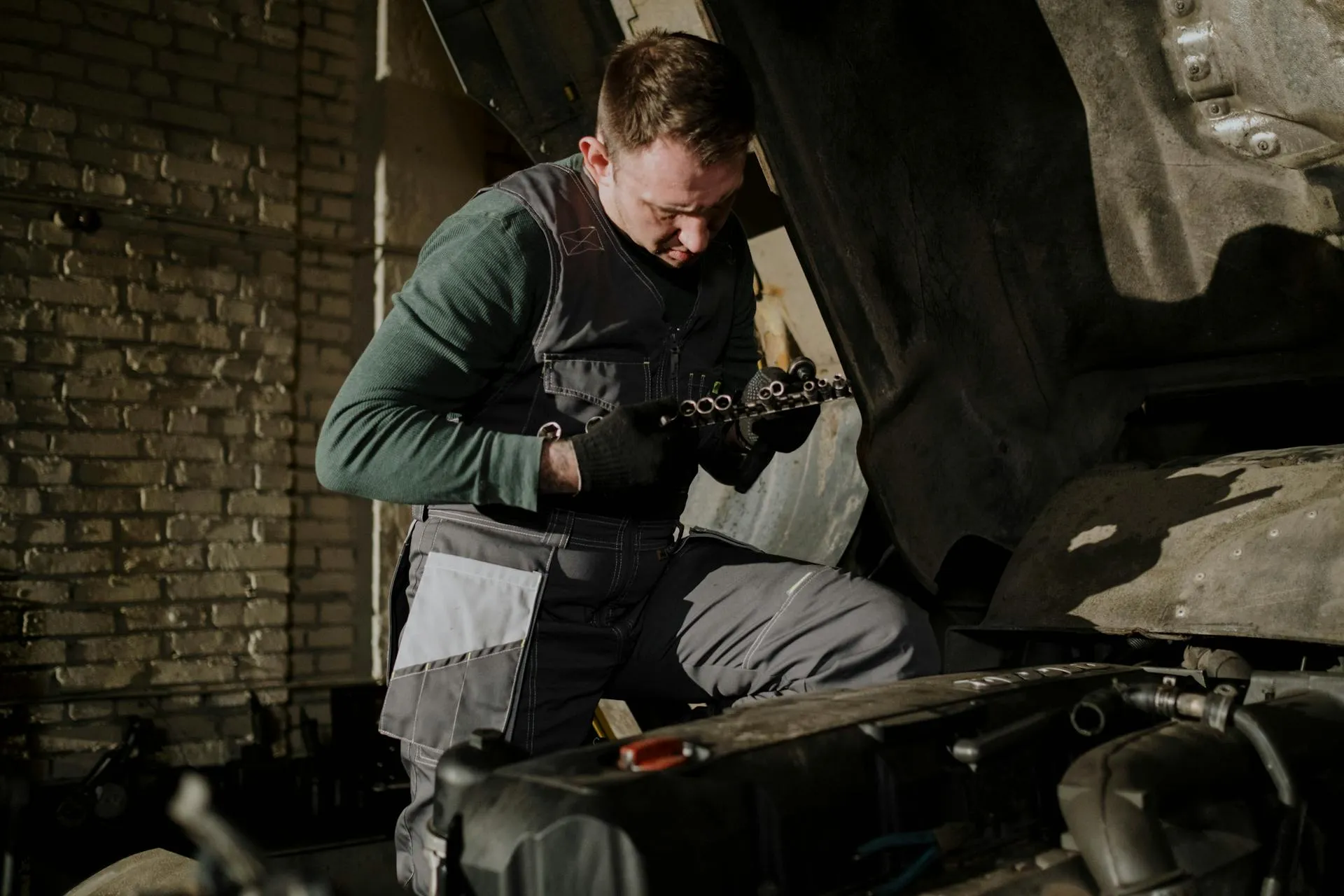 A mechanic performing engine repair on a car with the hood open, demonstrating professional automotive servicing by a BMW Specialist focused on engine diagnostics and maintenance.