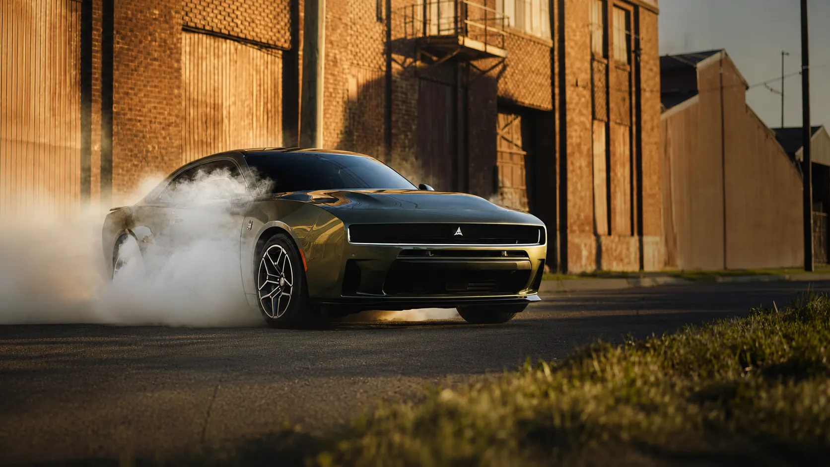 A dark green Dodge muscle car performs a smoky burnout on an urban industrial street at golden hour, with thick white tire smoke surrounding the rear wheels and brick warehouse buildings in the background. This dramatic image represents the power and performance associated with a professional Dodge repair center, highlighting expert maintenance and repair for Dodge vehicles.