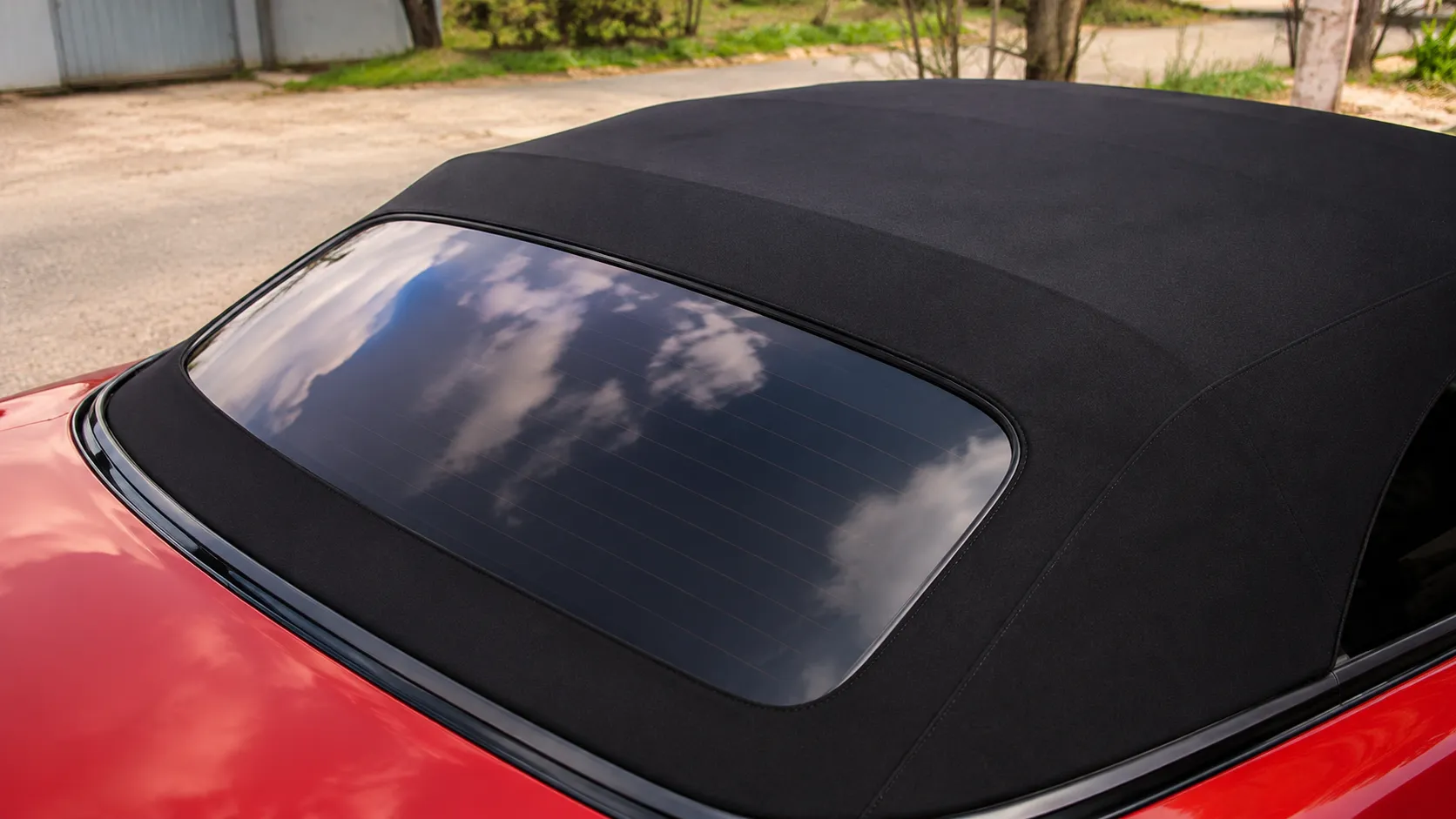 Close-up of a red convertible with a black fabric soft top and rear glass window, highlighting the condition and fit of the roof material. This image is ideal for illustrating convertible roof repairs near me, showcasing common areas where wear, damage, or replacement may be needed to restore the vehicle's appearance and weather protection.